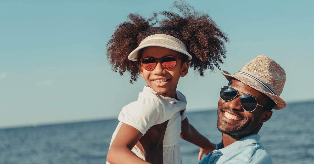 african-american-father-and-daughter-on-beach-wearing-sunglasses-and-hats