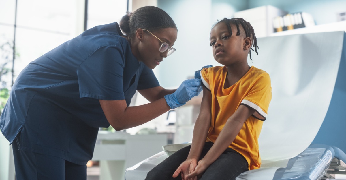 african american boy sitting in the chair in bright hospital female black nurse putting patch